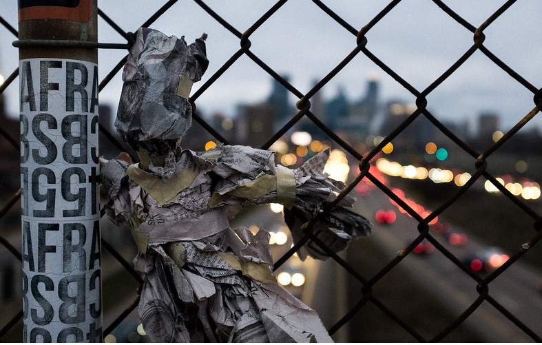Image of newspaper puppet on chain link fence over highway bridge