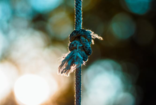 photo of vertical rope with frayed knot, blurred lighs in background