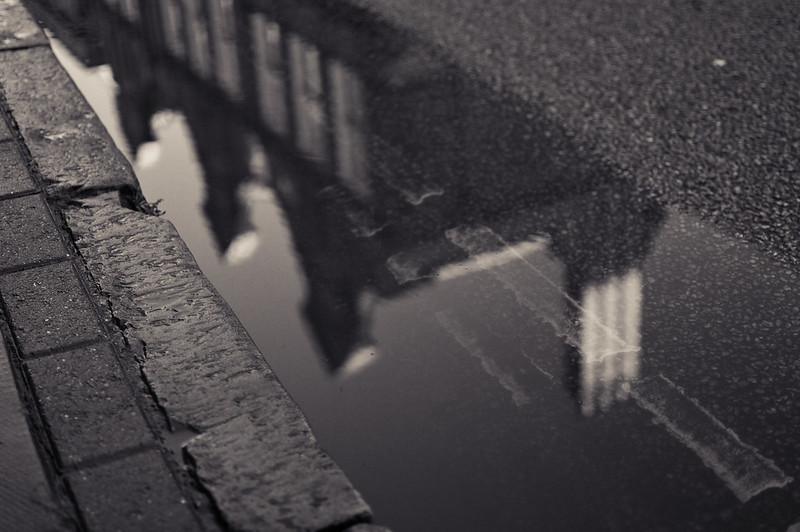 Image of old building reflected in pool of water by street curb