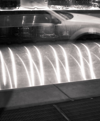 Multiple exposure image showign a row of bottles, a car, and blurred steaks of light above a patch of pavement and sidewalk grille.